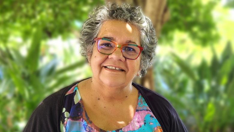 Smiling woman sitting under trees and surrounded by greenery in UQ gardens
